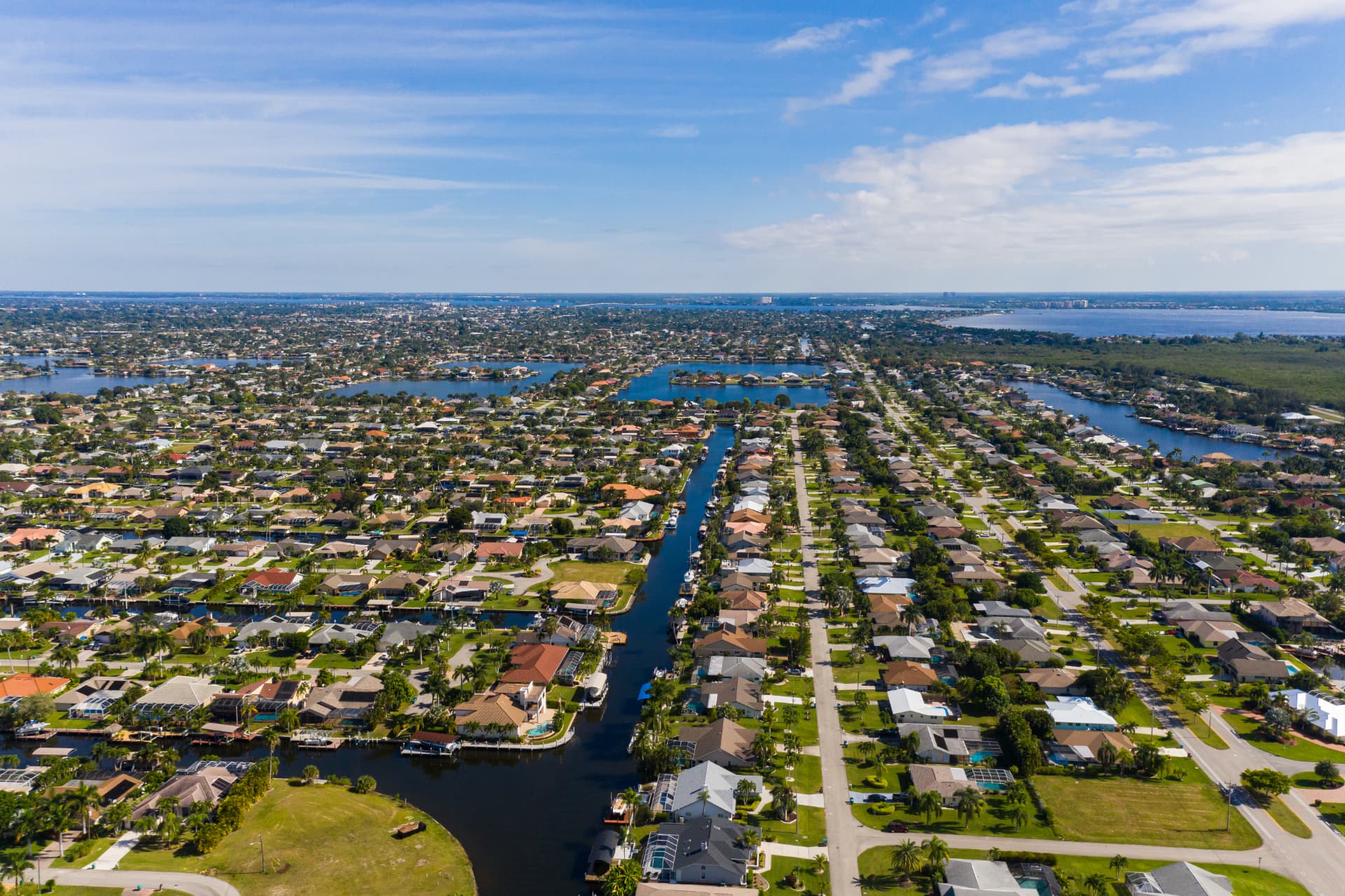 Daytime aerial view of Cape Coral, Florida, showing residential canals lined with single-family homes, boat docks and palm-lined streets