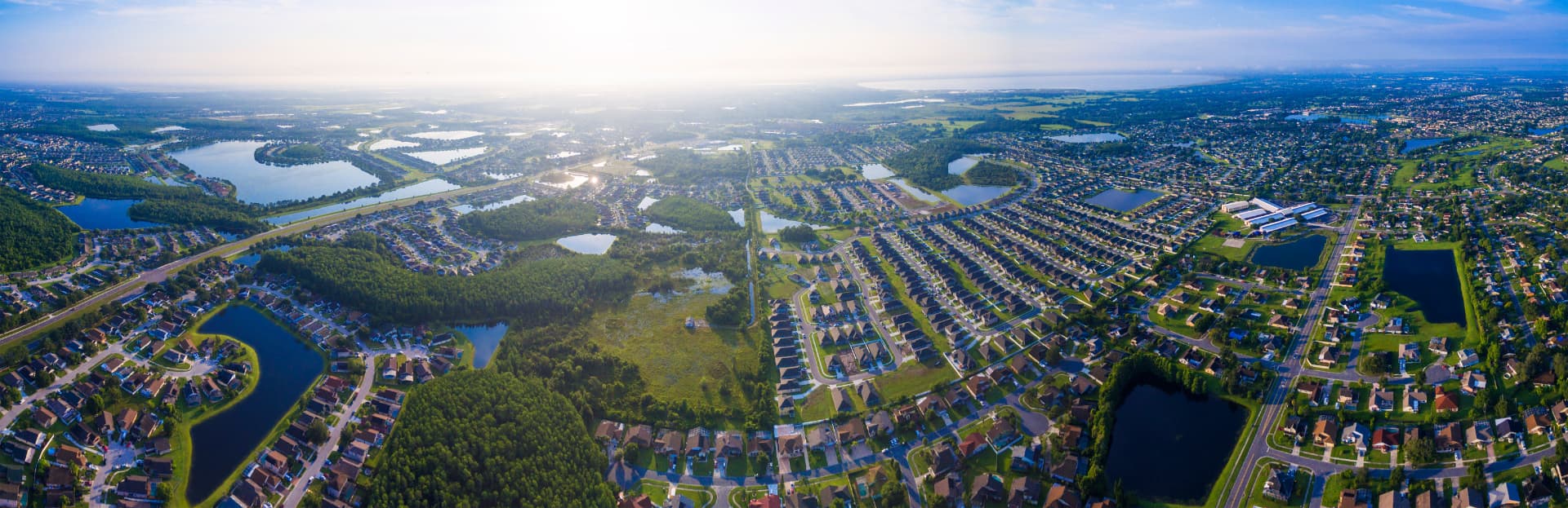 Wide morning aerial view of residential subdivisions, retention lakes and tree lines across the Kissimmee, Florida area